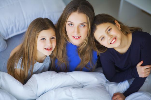 Happy family playing at home. mother and toddler daughters relaxing and having fun in bed in cozy weekend morning Premium Photo